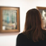 Brunette woman looking at artwork in museum. Rear view.